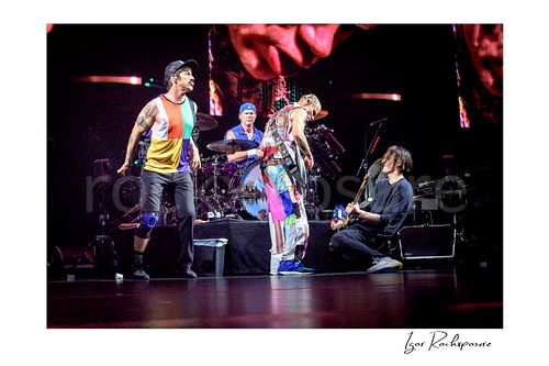 Horizontal color image of Anthony Kiedis, Chad Smith, Flea, and Josh Klinghoffer of Red Hot Chili Peppers performing live on stage, with Smith at the drum kit while the band gathers in a dynamic full-band concert moment