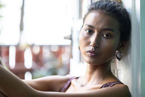 A portrait of a slender Indian woman in a purple top sitting on a chair on a balcony.