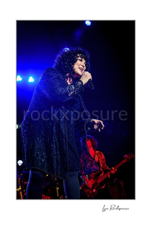 Vertical color image of Ann Wilson singing into a microphone during a Heart concert under vivid blue stage light