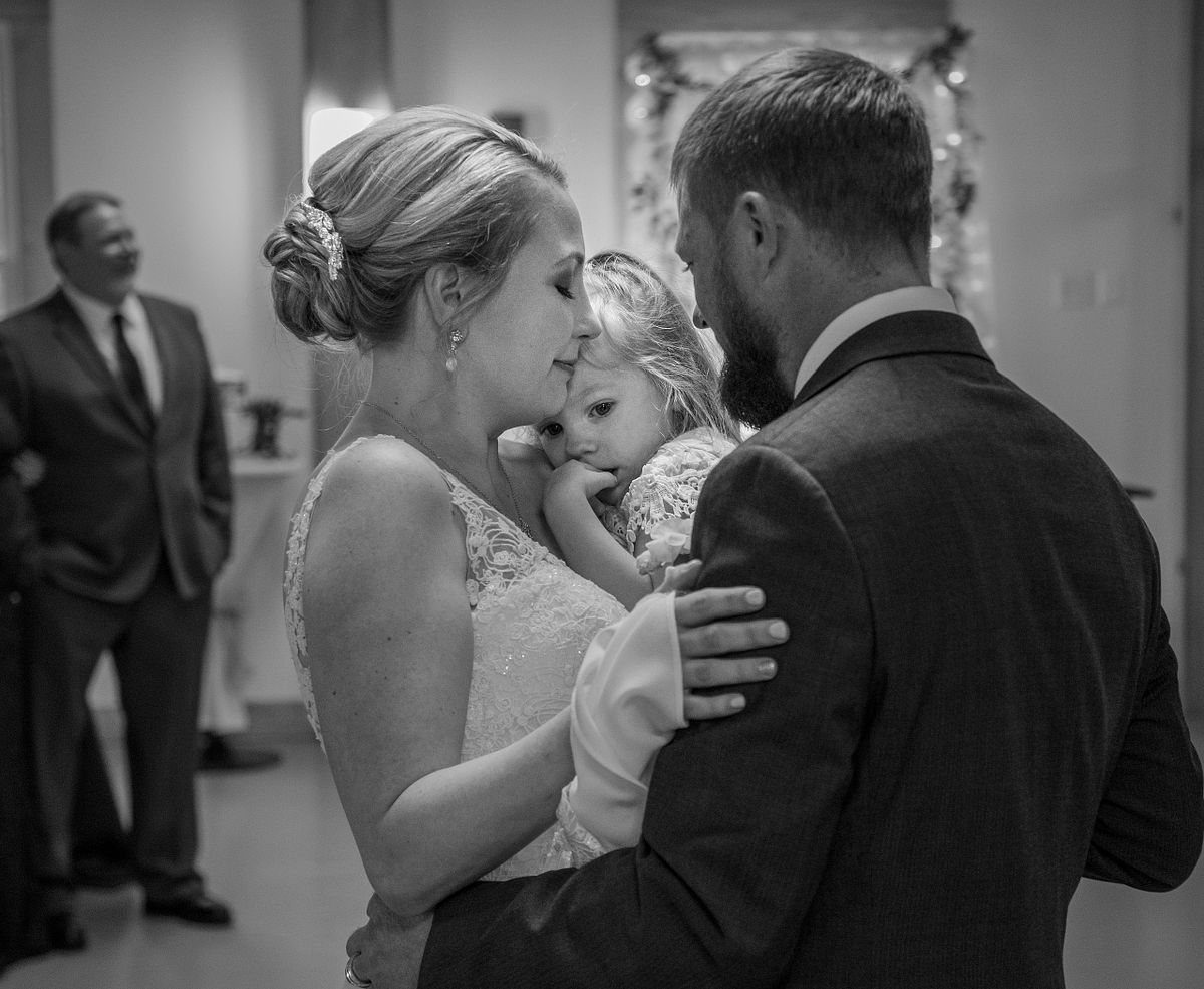 black and white photo of emotional first dance with the couple holding their young daughter while dancing