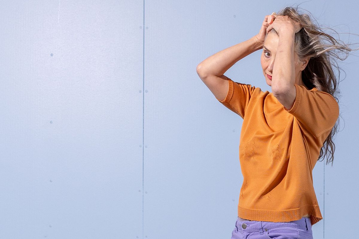 Woman in orange top with windblown hair against pastel blue wall, Stockholm environmental portrait