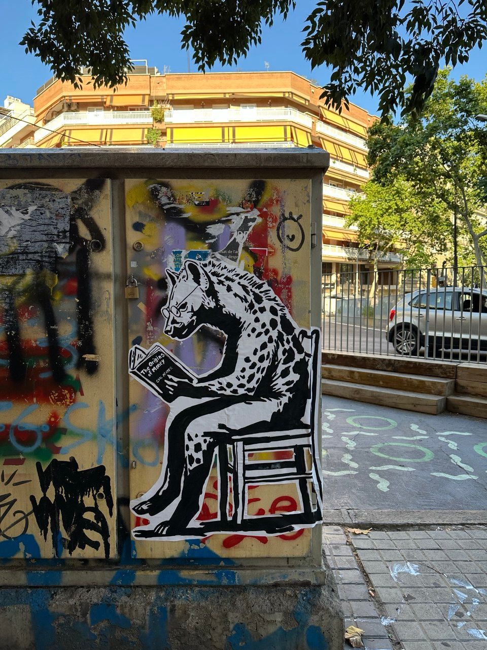 Street art stencil in Barcelona depicting a hyena wearing glasses, sitting on a chair and intently reading a book titled "THE ORIGINS OF MONEY" by Carl Menger. This piece by Street Cyber subtly promotes financial literacy, critical thinking about economic history, and the foundational knowledge needed to understand Bitcoin. It blends intellectual curiosity with raw street art.