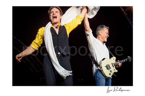 Horizontal color image of David Lee Roth and Eddie Van Halen of Van Halen celebrating on stage with raised hands and Eddie holding a white electric guitar