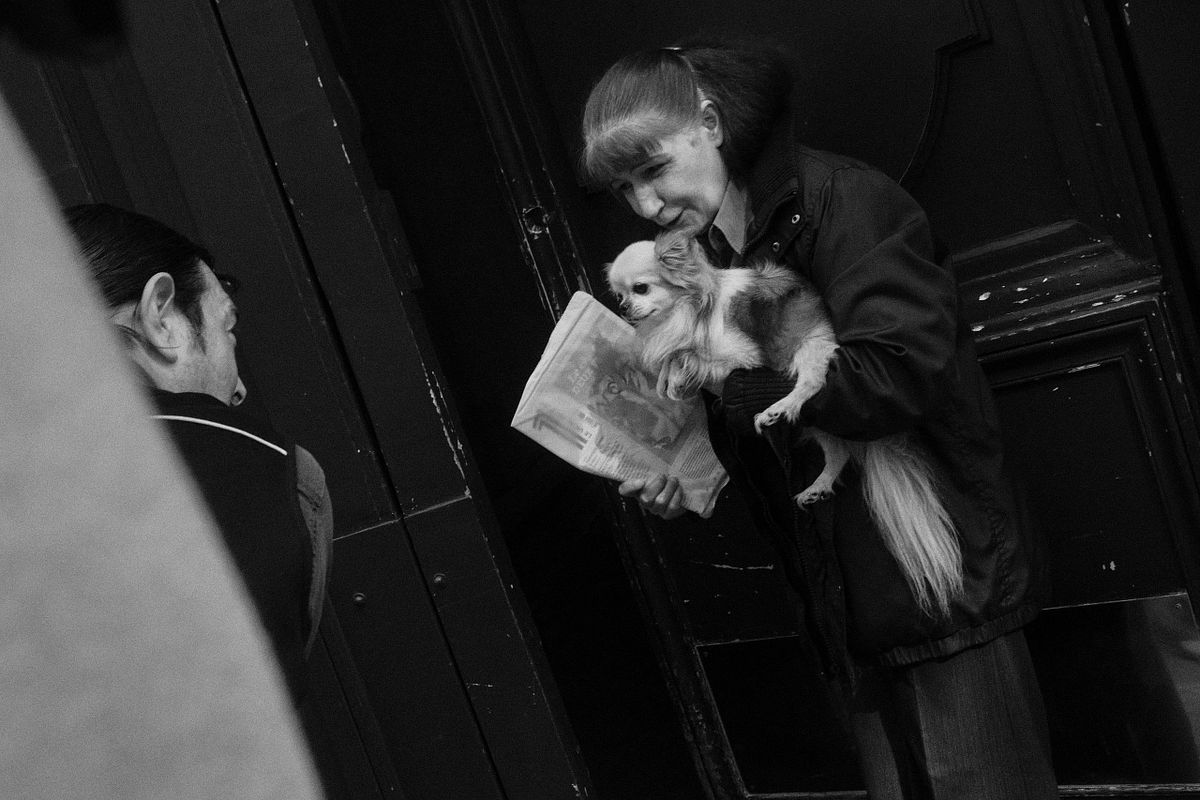 A woman holding a small dog and a newspaper on a Paris street, captured by photographer Sandeep Gajula