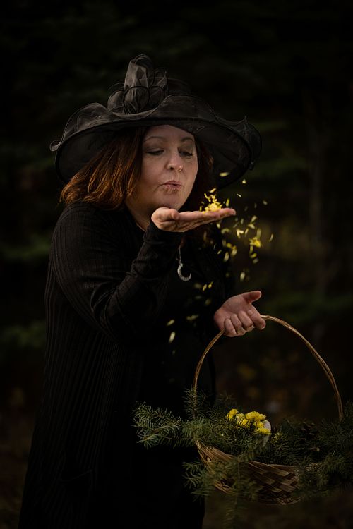 A witch blows yellow flower petals into the forest.