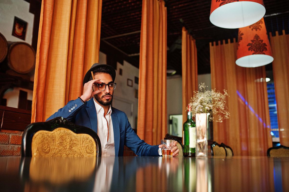 Handsome well-dressed arabian man with glass of whiskey and ciga
