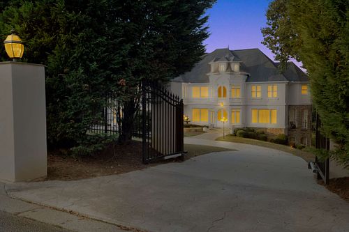 Spacious white mansion with illuminated windows and lush greenery