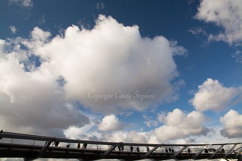 People walking across the Millennium Bridge under a blue sky