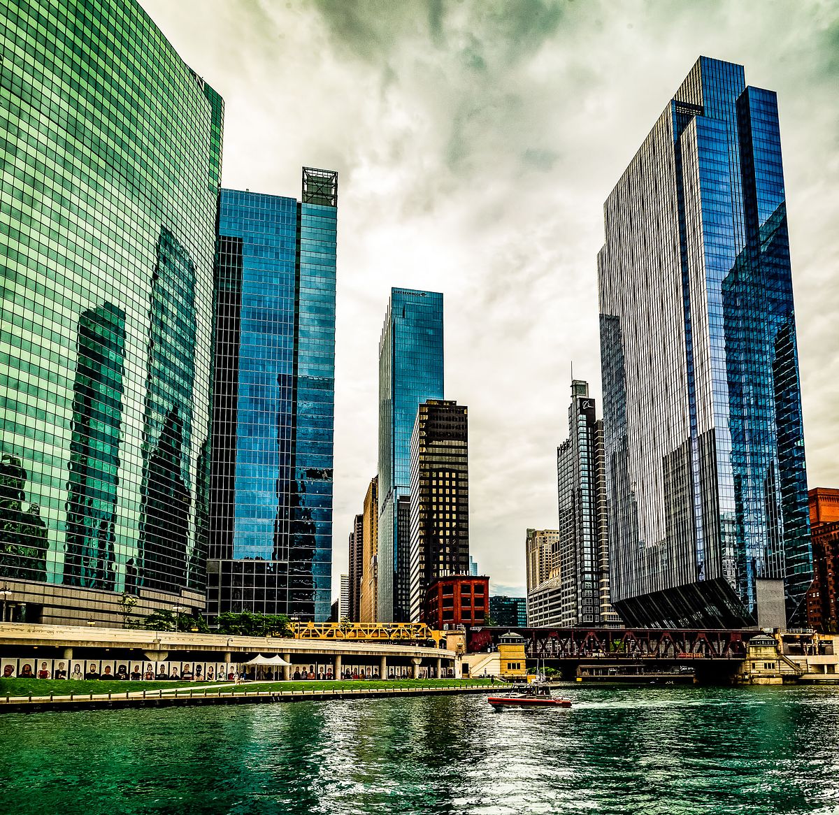 Skyscrapers tower over the Chicago River, their reflections shimmering on the water beneath looming clouds.