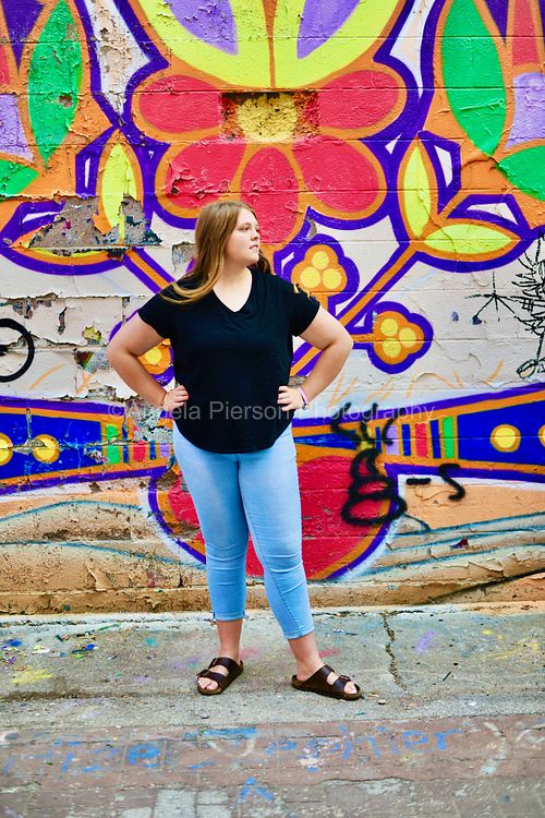 A young woman stands in front of a color graffiti wall
