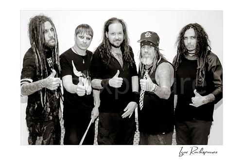 Horizontal black and white image of Korn members posing together in a backstage hallway portrait