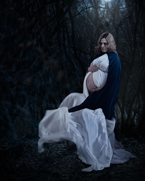 Expecting mother standing in a windy forest protecting her belly.