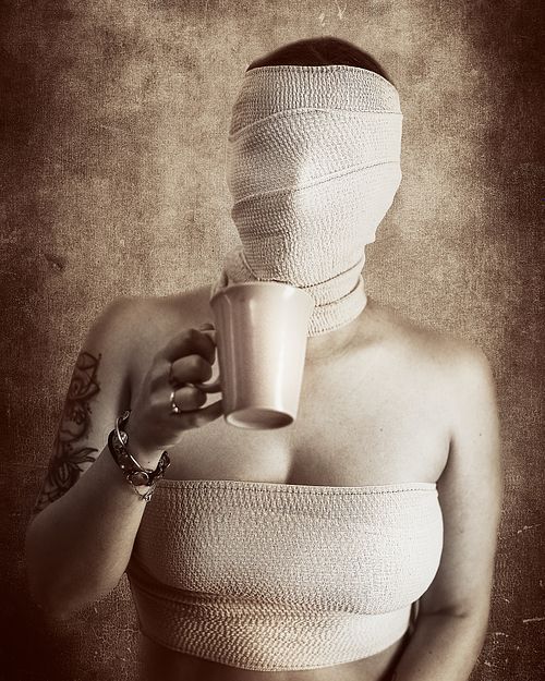 Portrait artistique d'une femme en bandages buvant une tasse de caf&eacute;, symbolisant la perte d'identit&eacute; et la r&eacute;silience silencieuse &mdash; photographie fine art Pascal Yennis, Namur, Belgique.