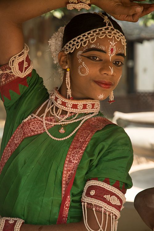A young man in traditional dress and painted face performs a lively folk dance outside the National Crafts Museum in Delhi, India, showcasing his heritage.