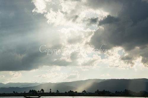 Sunbeams at twilight with Intha fisherman in a canoe-like boat