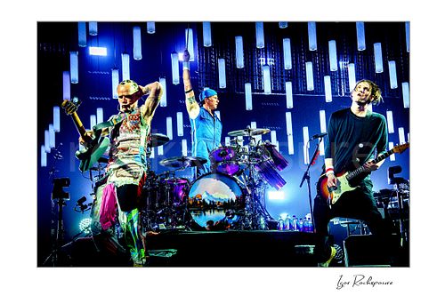 Red Hot Chili Peppers Live Concert Print  Horizontal color image of Flea, Chad Smith, and Josh Klinghoffer of Red Hot Chili Peppers performing live on stage, with Smith raising one arm at the drum kit beneath a glowing LED light backdrop