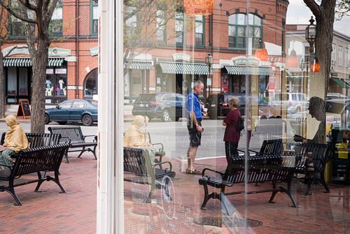 Reflections of diverse shoppers and a New England suburban shopfront, depicting community unity and connection.