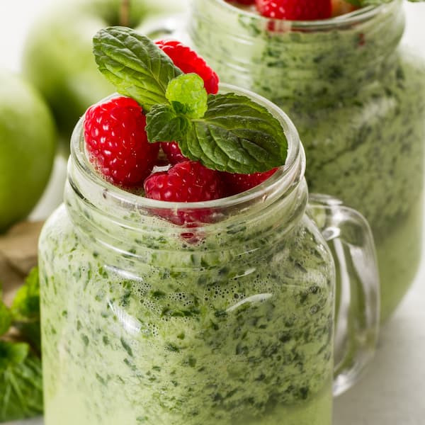 mason jars with green smoothies topped with berries and mint