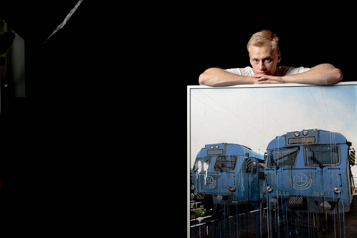 Male artist leaning on painting of blue trains, Stockholm portrait photographer