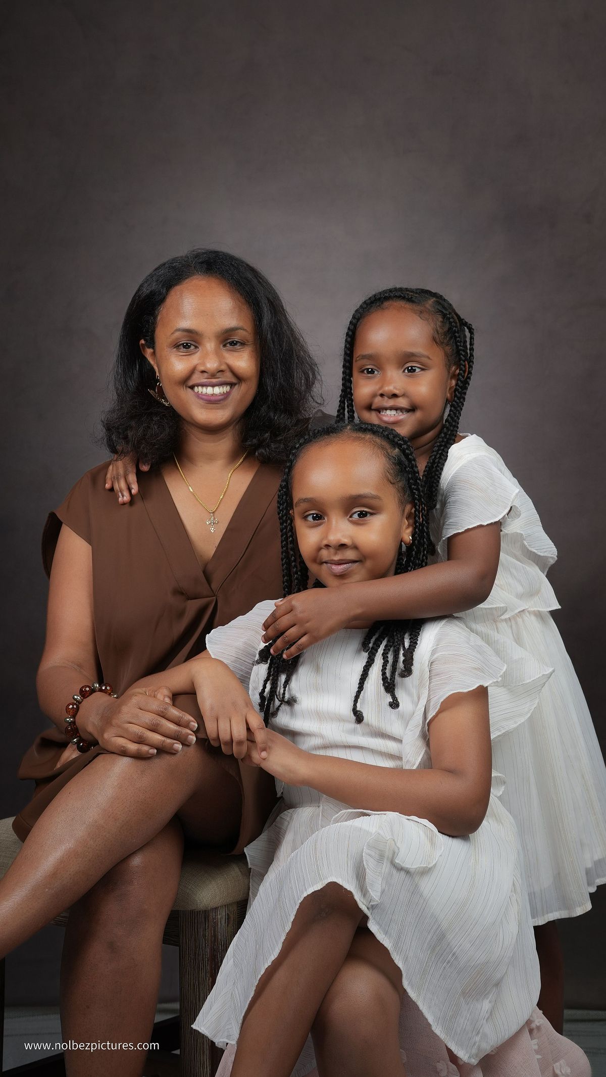 A studio portrait of a mother wearing a brown dress with her two young daughters