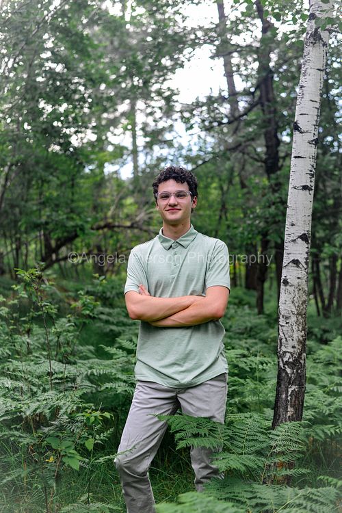 a young man stands in a tree grove with green ferns