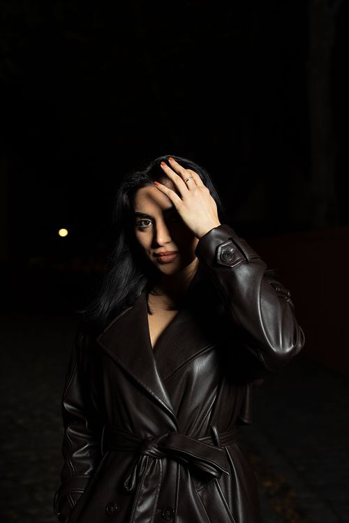 Nära porträtt av skådespelare i kvällsljus med hand mot pannan och skuggspel över ansiktet, mörk bakgrund.