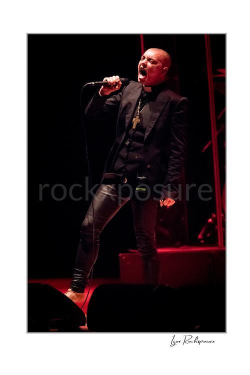Vertical color image of Sinéad O’Connor singing into a microphone on stage under red lighting