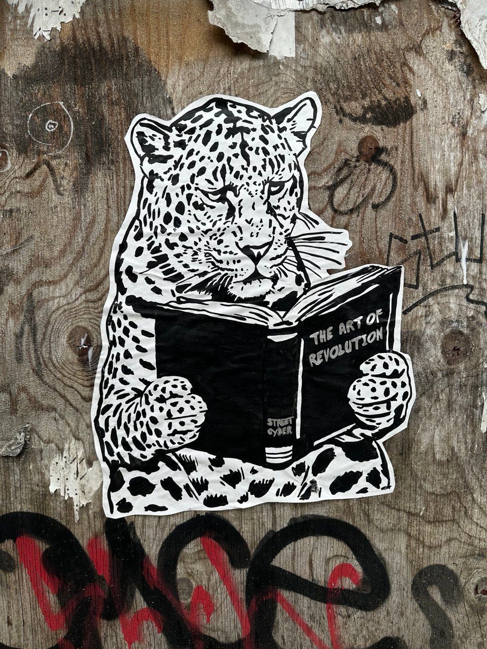 Street art stencil in Amsterdam depicting a leopard wearing glasses and intently reading a book titled "THE ART OF REVOLUTION" by STREET CYBER. This powerful piece symbolizes the pursuit of knowledge as the true catalyst for change and freedom, directly referencing Street Cyber's foundational exhibition and brand philosophy.