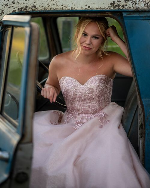 A blond graduating student from Prince Albert sitting in a baby blue vintage truck in her pink gown.