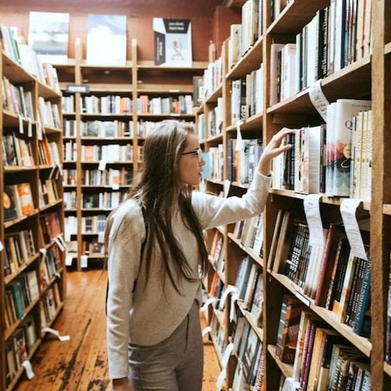 woman searching library books with multiple full shelves surrounding her