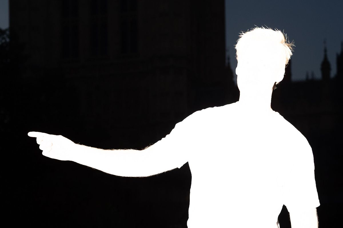 &Ouml;verexponerad silhuett av en person som pekar &aring;t v&auml;nster mot en m&ouml;rk bakgrund, ett grafiskt och experimentellt portr&auml;tt.