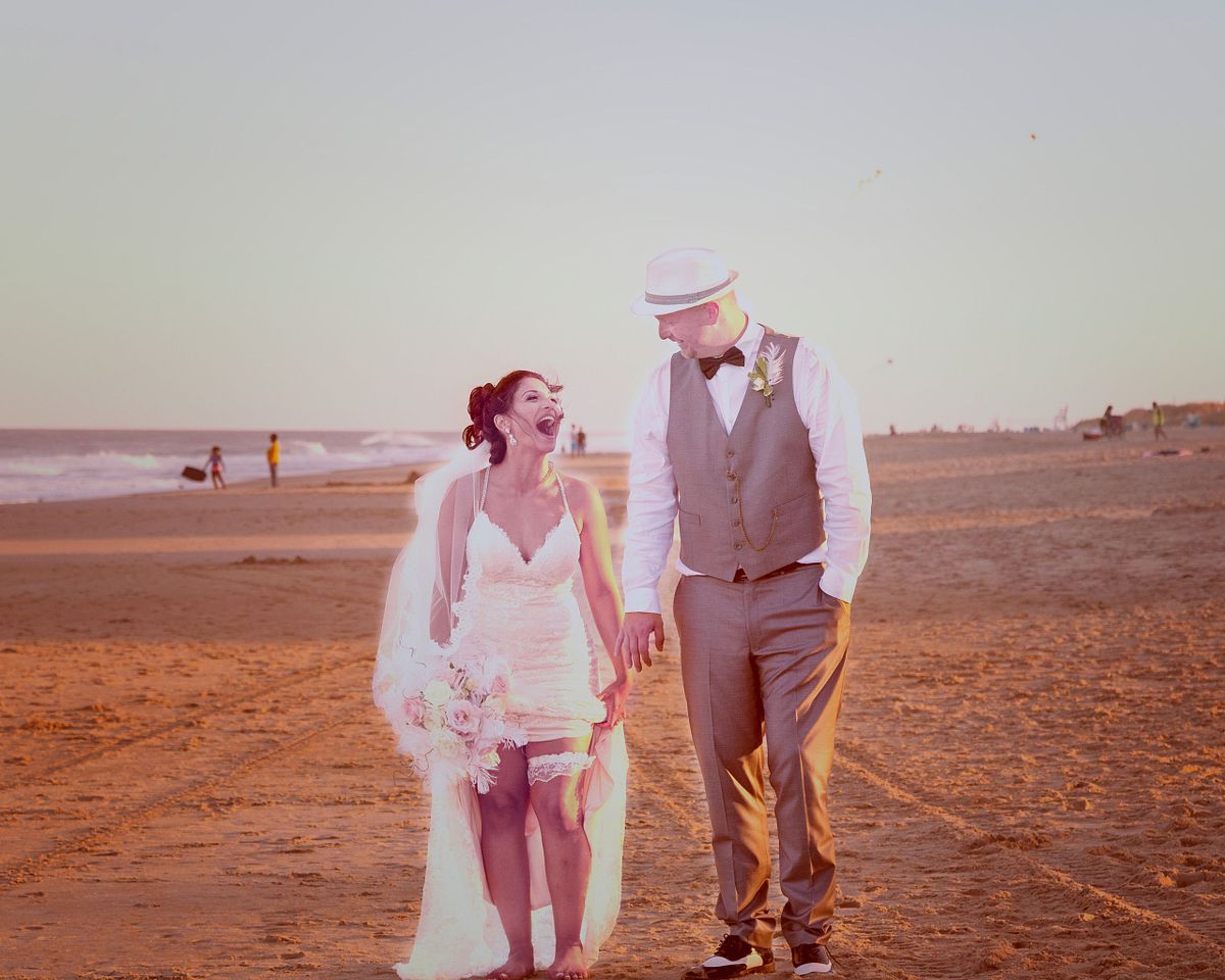 a bride is laughing showing off the garter belt on the beach in sussex county, de,the sun is setting and the the weather is warm