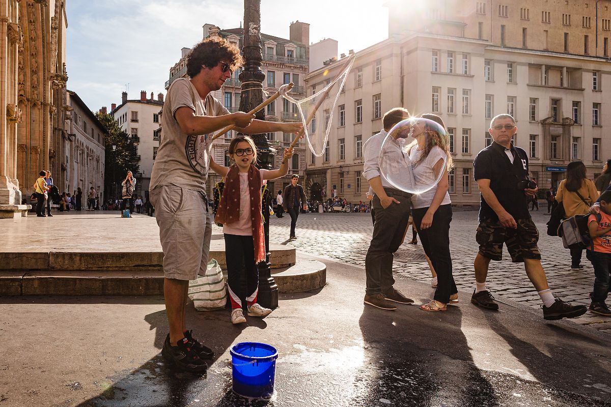 Tarif Photographe Mariage - Sebastien CLAVEL Photographe - Sc&egrave;ne de rue &agrave; Lyon avec un artiste de bulles et un couple s'embrassant, un moment plein de magie et de vie urbaine