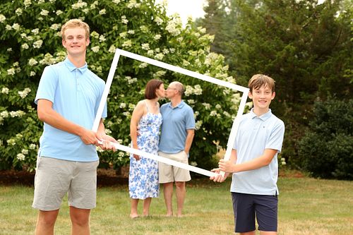 Two teenage boys hold up large frame to show mom and dad in the background