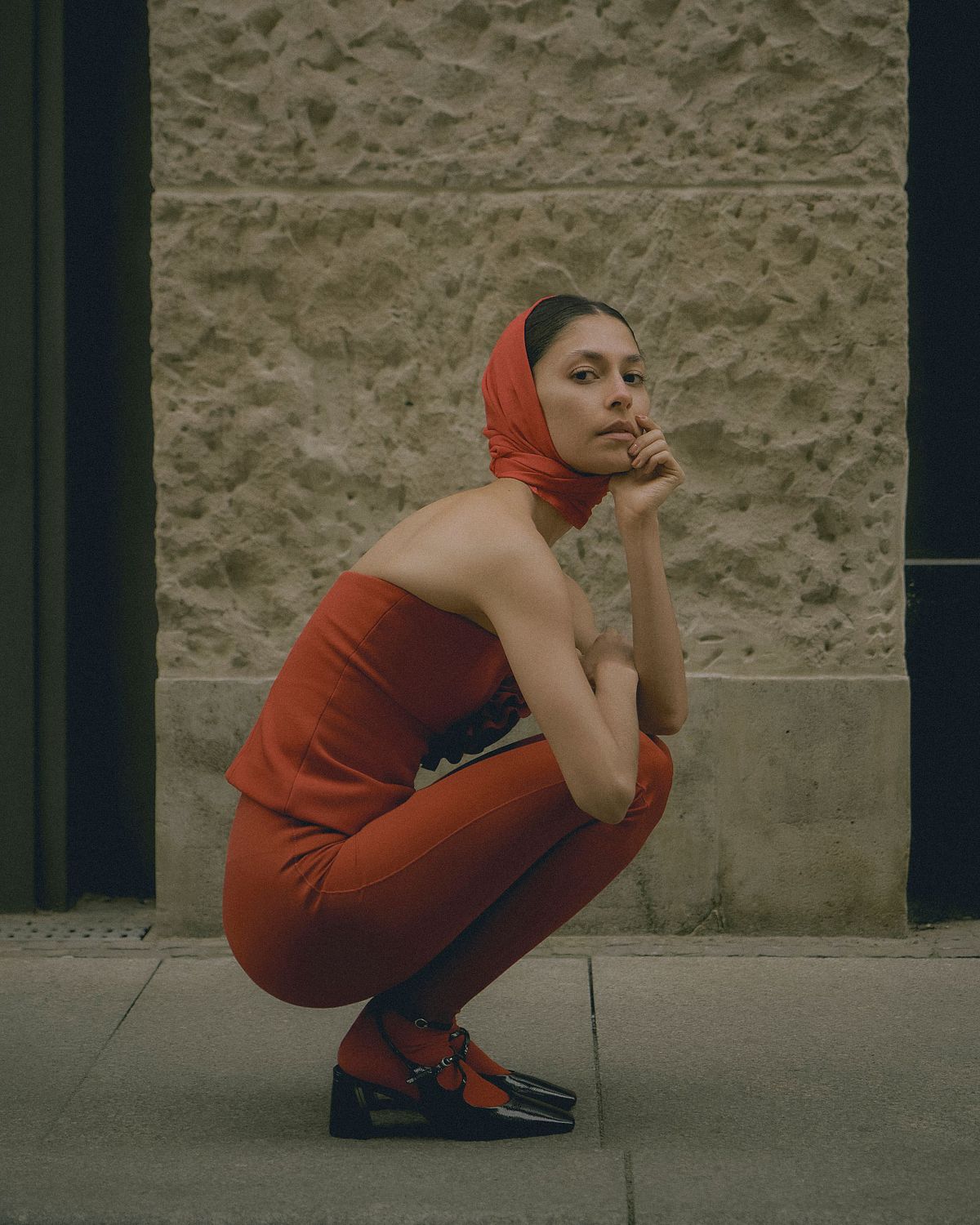 Portrait of a female model wearing a total red outfit inspired by Magda Butrym in a sitting pose in the streets of Leipzig. Photographed by Filianna Karamanli.