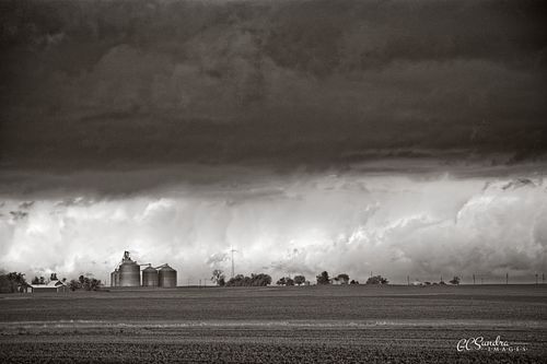 "Caught in the Middle" is a rural landscape of grain elevators in Marshall County, Illinois waiting for the storm clouds to dump on them on this spring afternoon. This fine art black and white print is copyrighted by Gregory C. Sundra and GC Sundra IMAGES, LLC.