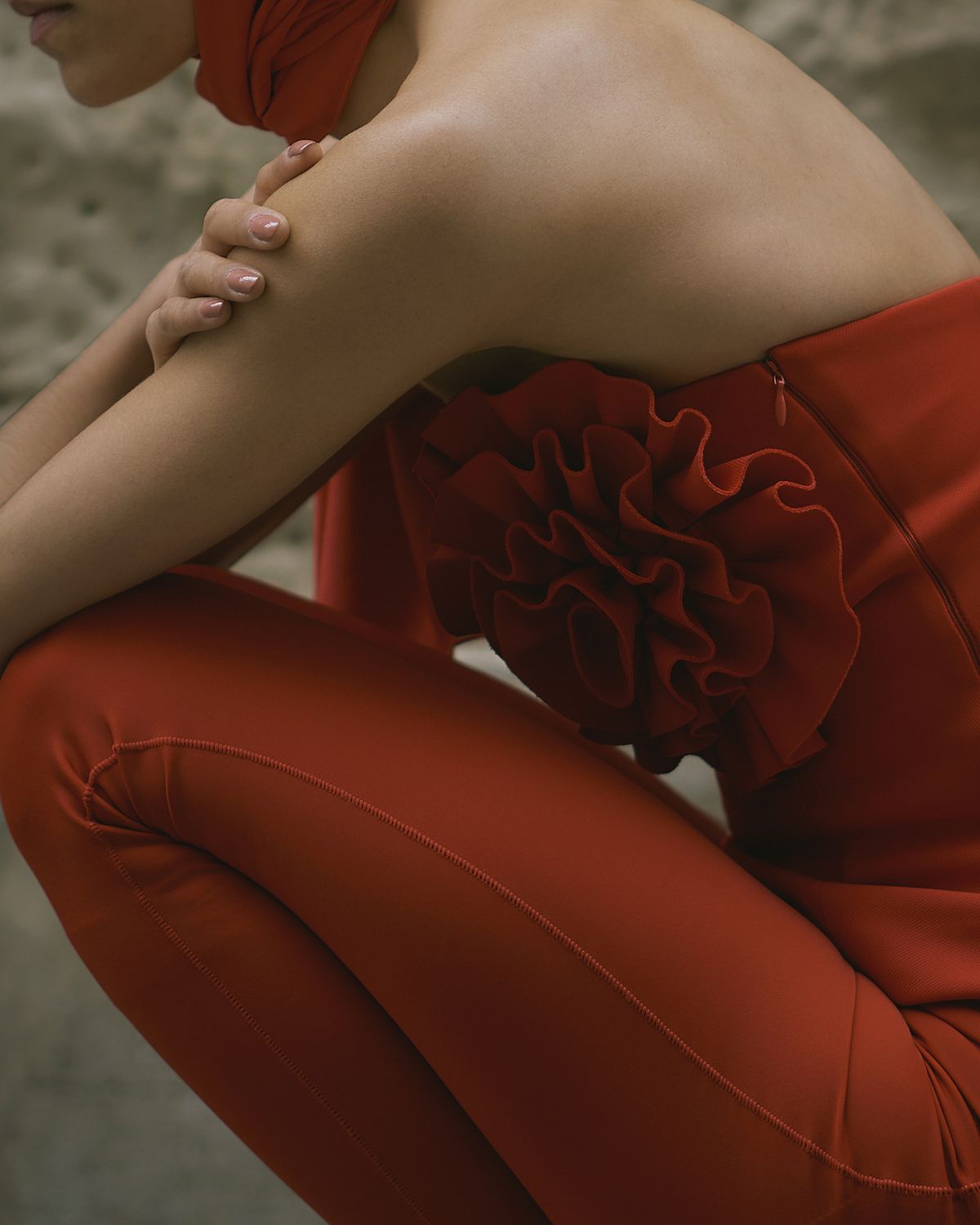 Close up of a female model wearing a total red outfit with a top with a statement flower inspired by Magda Butrym in a sitting pose in the streets of Leipzig. Photographed by Filianna Karamanli.