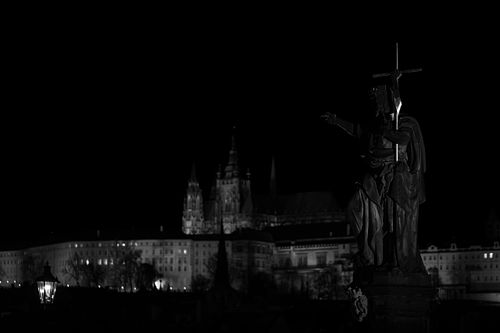 Statue du pont Charles pointant vers le château de Prague, photographie noir et blanc nocturne.