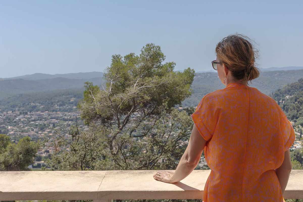 Kvinna i orange kl&auml;nning lutar sig mot en mur och ser ut &ouml;ver dalg&aring;ng och berg i bakgrunden.