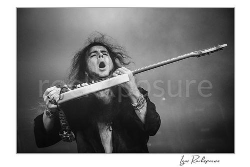 Yngwie Malmsteen Live Concert Print  Horizontal black and white image of Yngwie Malmsteen in a dramatic live performance close-up, holding a white guitar across his chest with mouth open amid stage haze