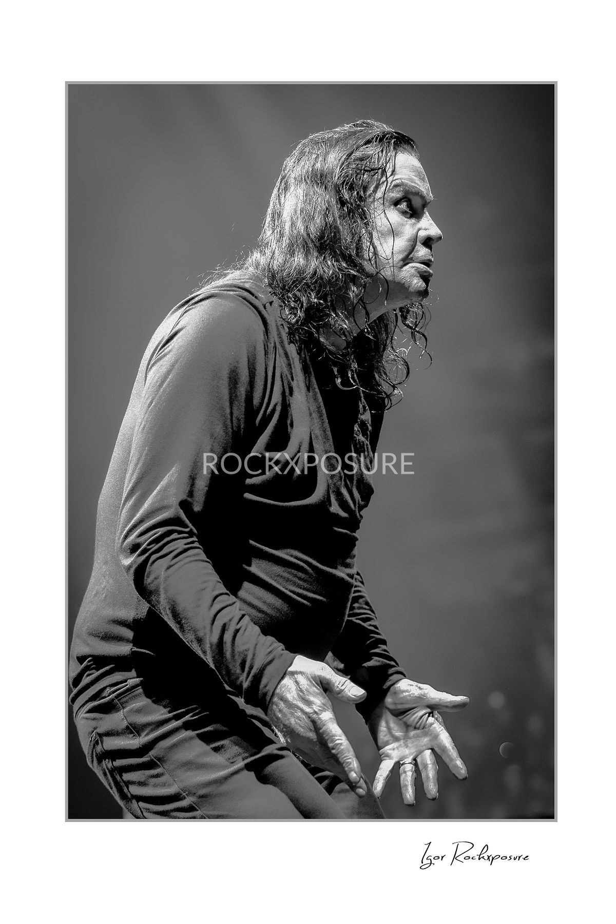 Black and white portrait of Ozzy Osbourne of Black Sabbath standing in profile with intense expression during a live performance