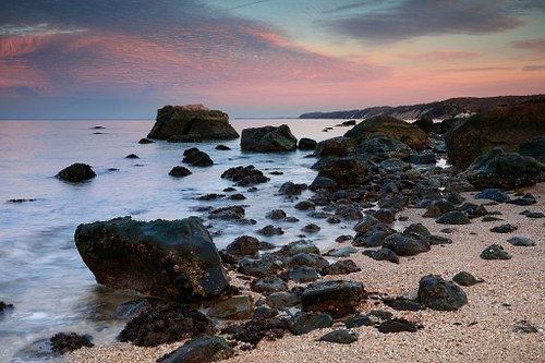 Pink clouds arch above dramatic coastline view.